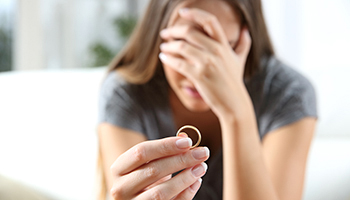 A woman holds a ring in front of her face, expressing sadness