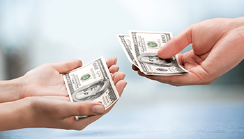 Two hands are positioned facing each other, each holding a stack of money, symbolizing an exchange